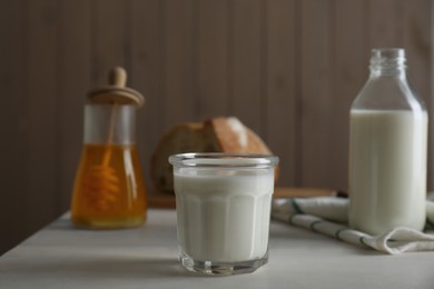Photo of Glass and bottle of milk, honey with bread on white wooden table