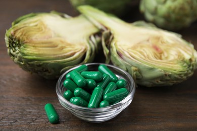 Bowl with pills and fresh artichokes on wooden table, closeup