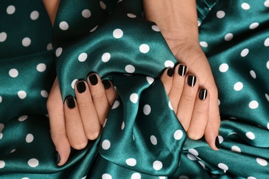 Photo of Woman with black manicure holding color fabric, top view. Nail polish trends