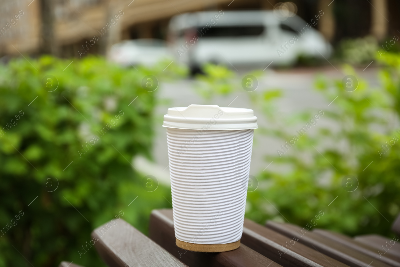 Photo of Paper cup of coffee on wooden bench outdoors. Takeaway drink