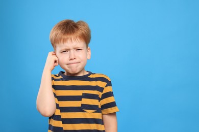 Photo of Little boy suffering from ear pain on light blue background. Space for text