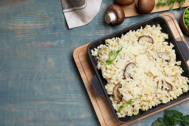 Photo of Delicious risotto with cheese and mushrooms on light blue wooden table, flat lay. Space for text