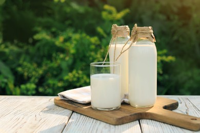 Photo of Bottles and glass of tasty fresh milk on white wooden table outdoors, space for text