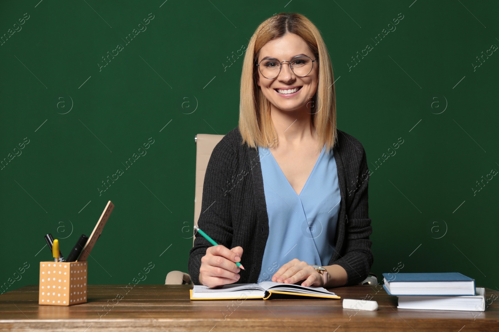 Photo of Portrait of beautiful teacher sitting at table near chalkboard