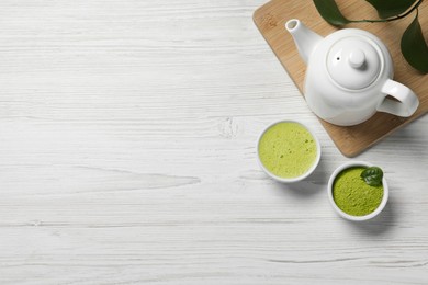 Cup of fresh matcha tea, teapot and green powder on white wooden table, flat lay. Space for text