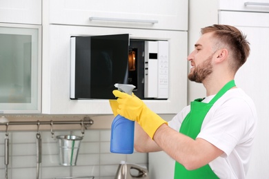 Photo of Young man in uniform cleaning microwave oven in kitchen