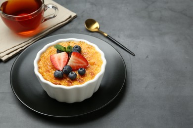 Photo of Delicious creme brulee with berries and mint in bowl on grey table. Space for text