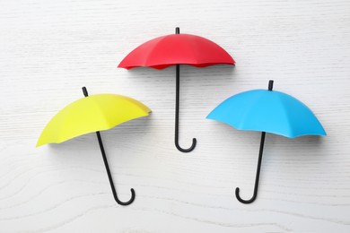 Small color umbrellas on white wooden background, flat lay