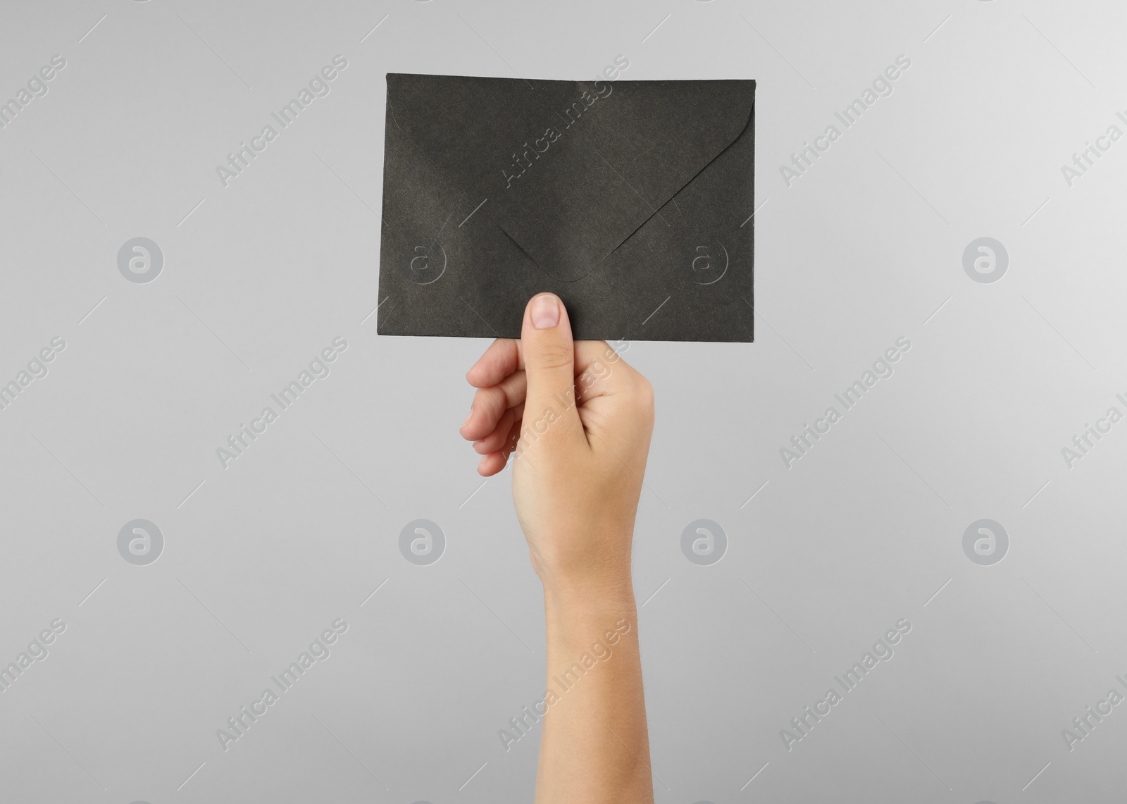 Photo of Woman holding black paper envelope on light grey background, closeup