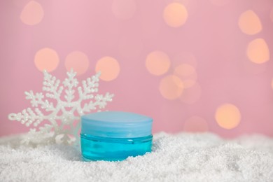 Photo of Jar of hand cream and decorative snowflake on snow against blurred lights, space for text. Winter skin care