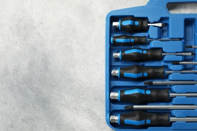 Photo of Set of screwdrivers in open toolbox on light grey textured table, top view. Space for text