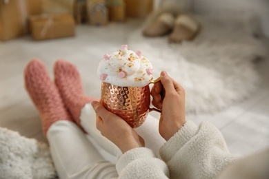 Photo of Woman holding cup of delicious drink with whipped cream and marshmallows indoors, closeup. Christmas celebration