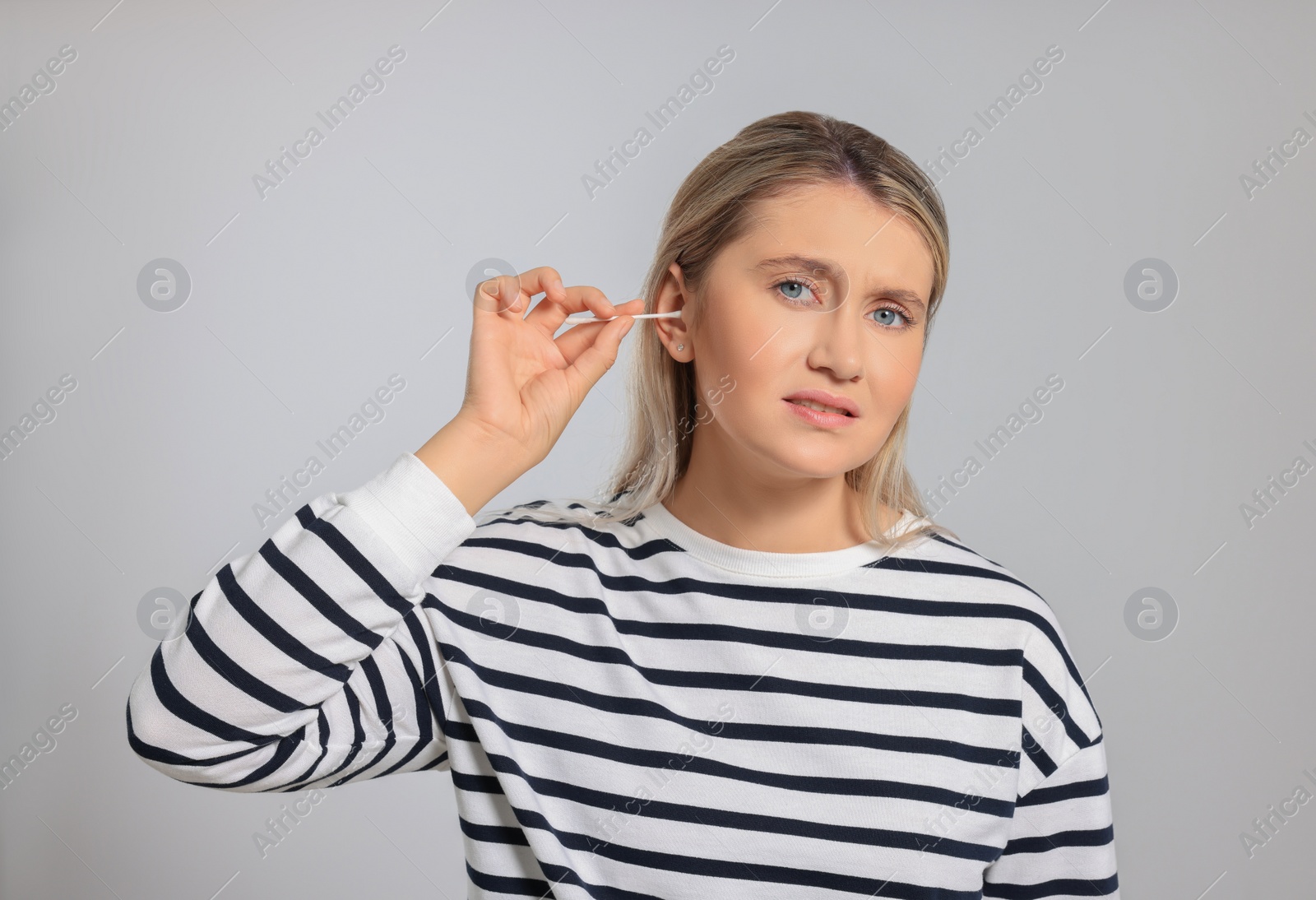 Photo of Young woman cleaning ear with cotton swab on light grey background