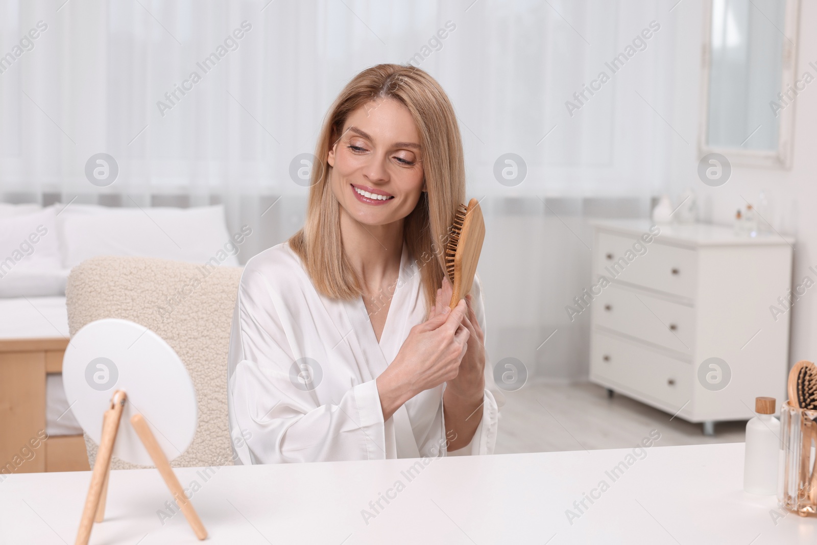 Photo of Beautiful woman brushing her hair at vanity in bedroom