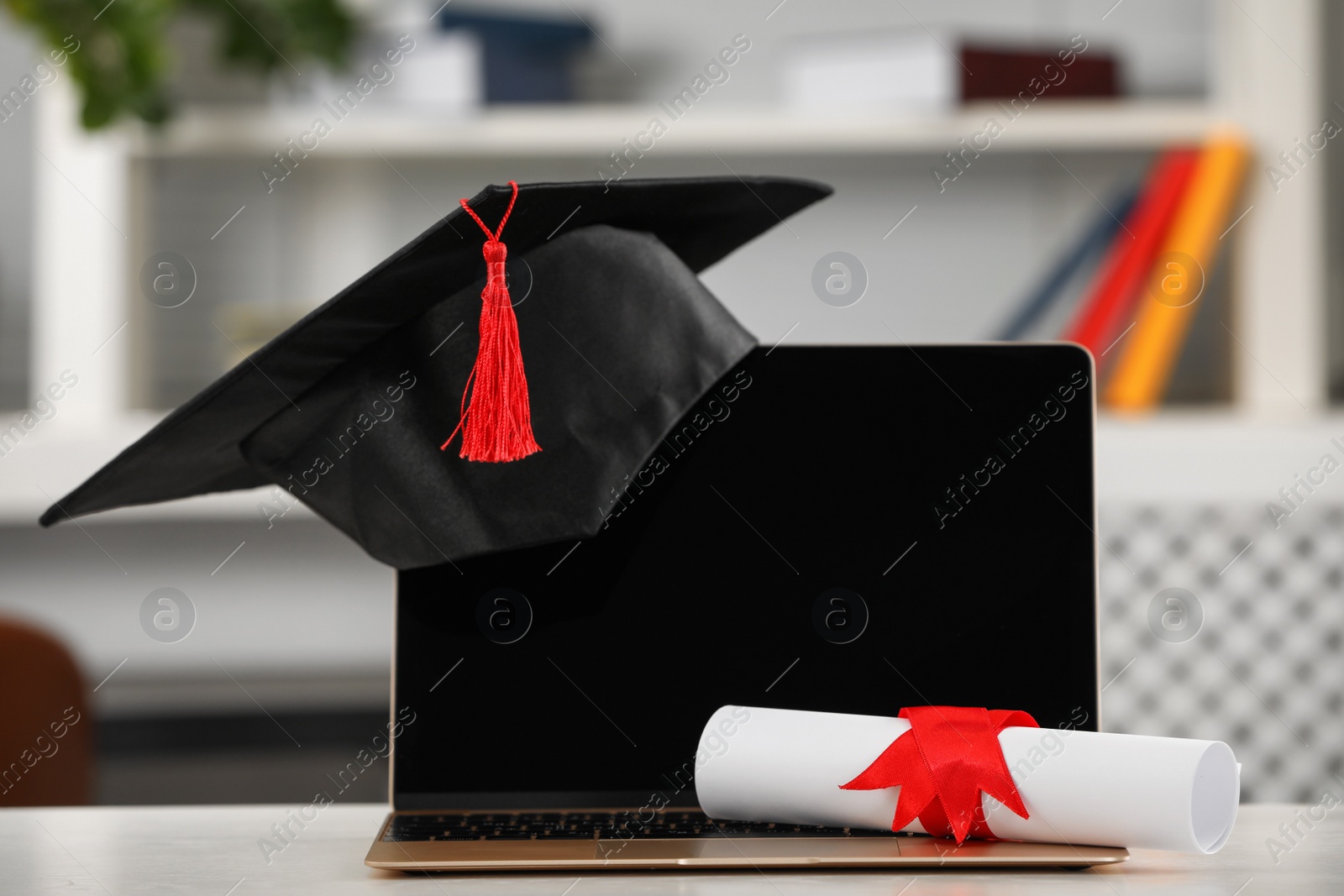 Photo of Graduation hat, student's diploma and laptop on white table indoors