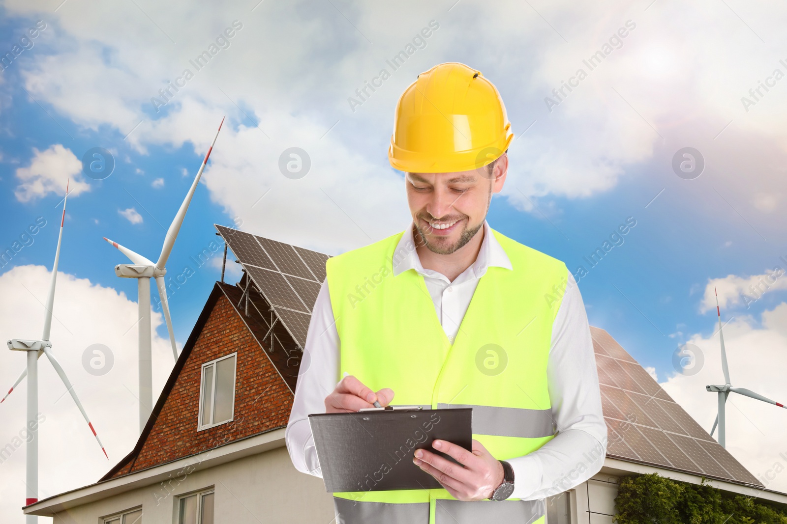 Image of Industrial engineer in uniform and view of wind energy turbines near house with installed solar panels on roof