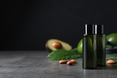 Bottles of avocado essential oil and almonds on grey table, space for text
