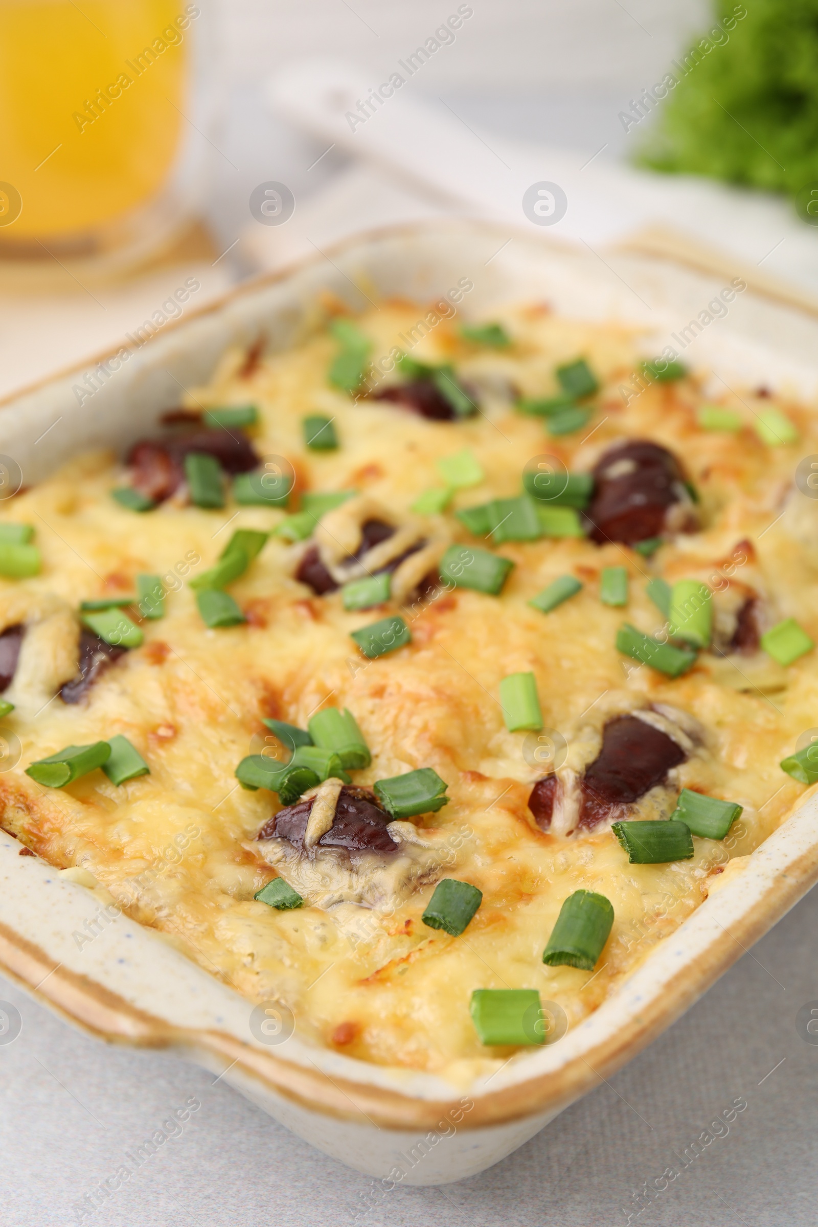 Photo of Tasty sausage casserole with green onions in baking dish on white table, closeup