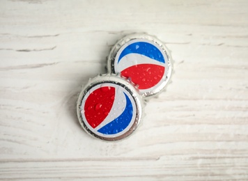 Photo of MYKOLAIV, UKRAINE - FEBRUARY 11, 2021: Pepsi lids with water drops on white wooden table, flat lay