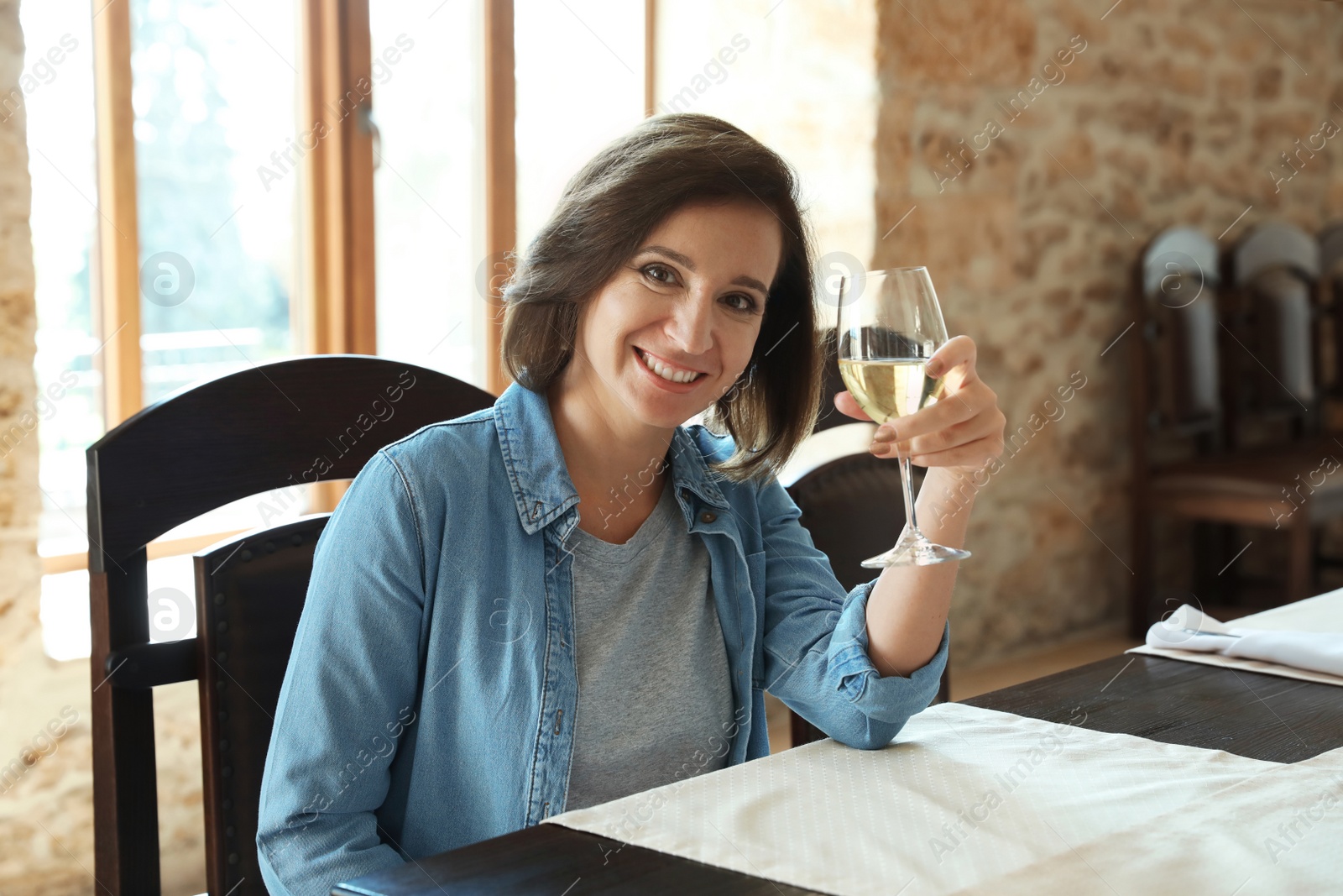 Photo of Woman with glass of white wine at table indoors