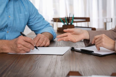 Senior man signing document in lawyer's office