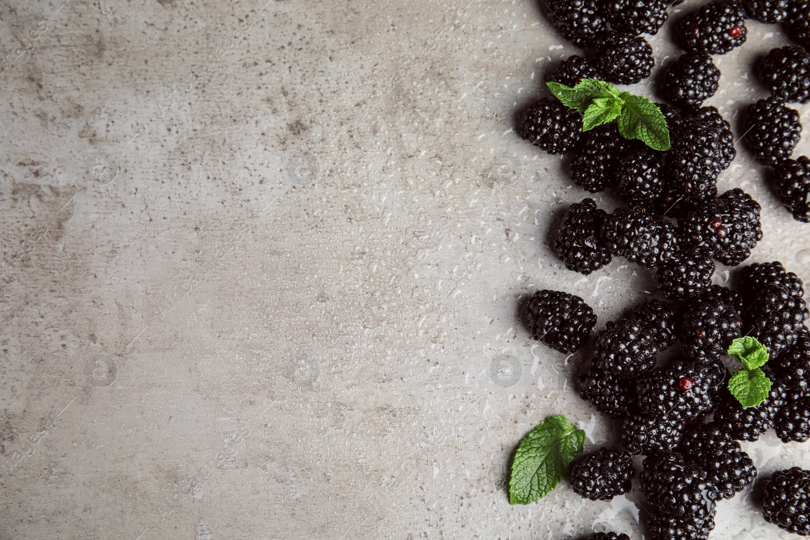 Photo of Tasty ripe blackberries with mint on grey table, flat lay. Space for text