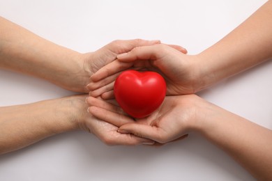 Photo of Young and elderly women holding red heart on white background, top view