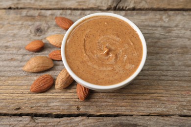 Delicious nut butter in bowl and almonds on wooden table, closeup