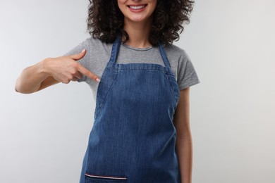 Photo of Woman pointing at kitchen apron on light grey background, closeup. Mockup for design