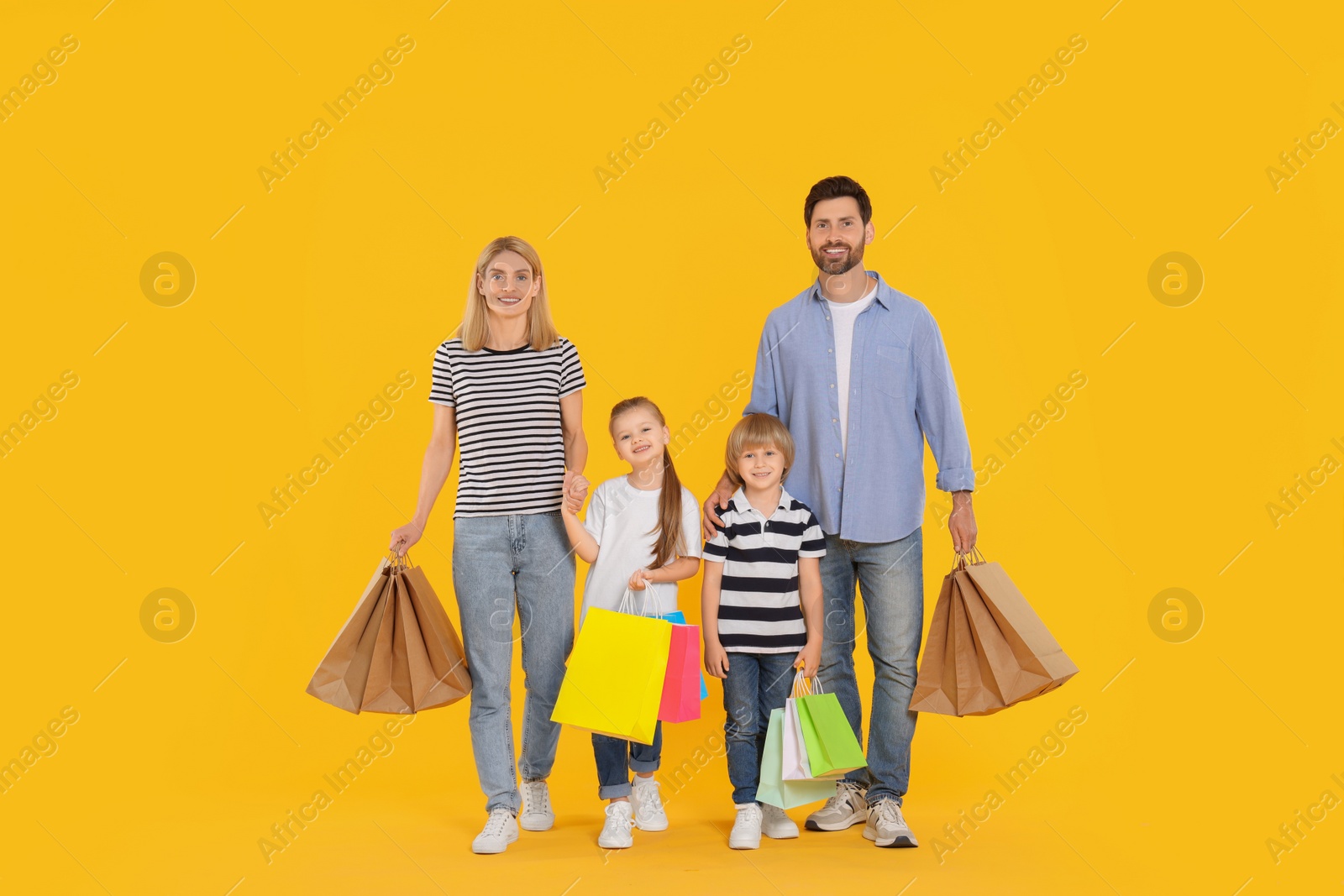 Photo of Family shopping. Happy parents and children with many colorful bags on orange background