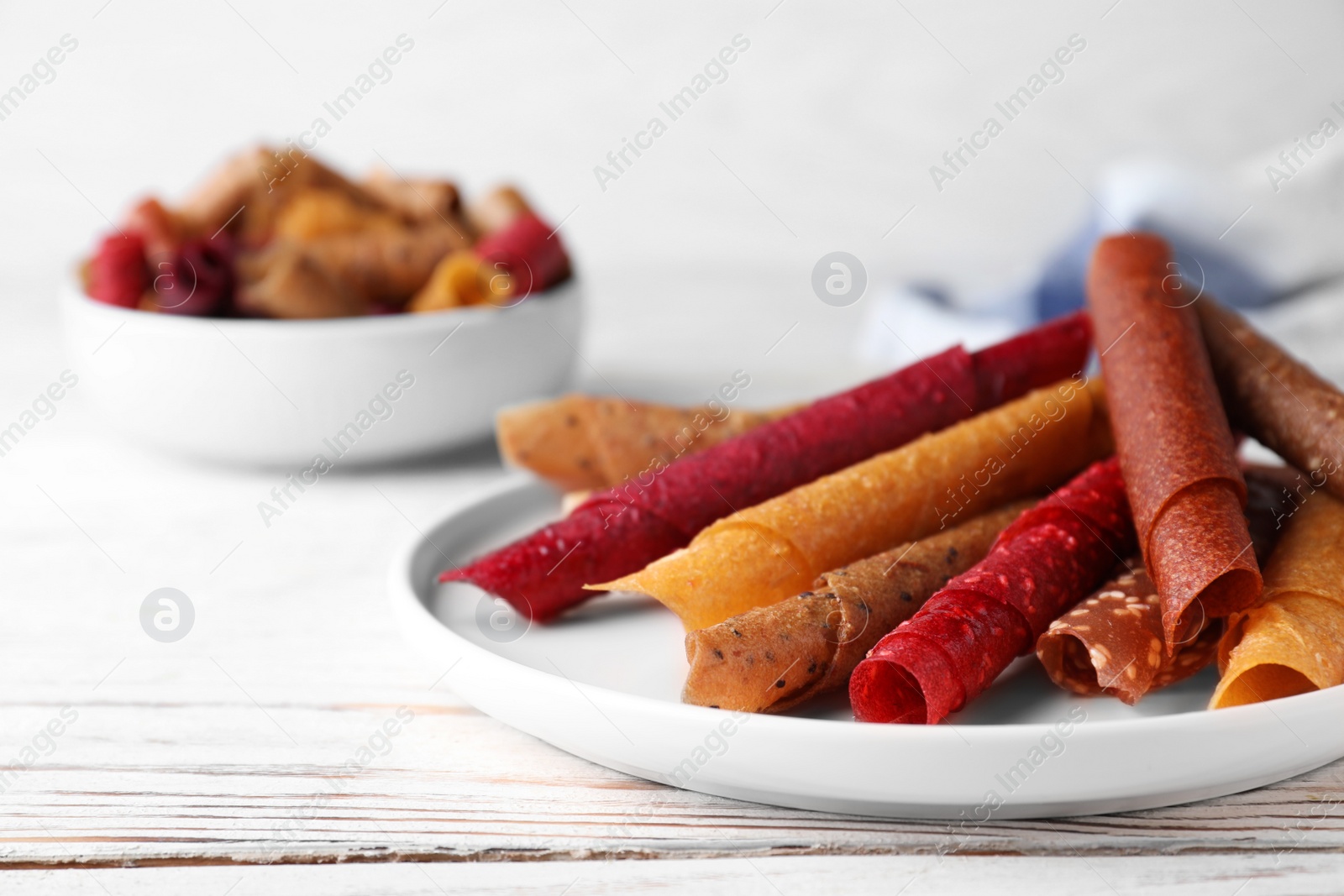 Photo of Delicious fruit leather rolls on white wooden table, closeup