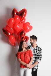 Photo of Happy young couple with heart shaped balloons on light background. Valentine's day celebration