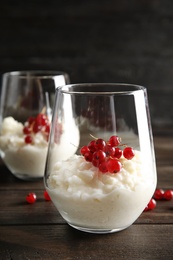 Photo of Creamy rice pudding with red currant in glass on wooden table