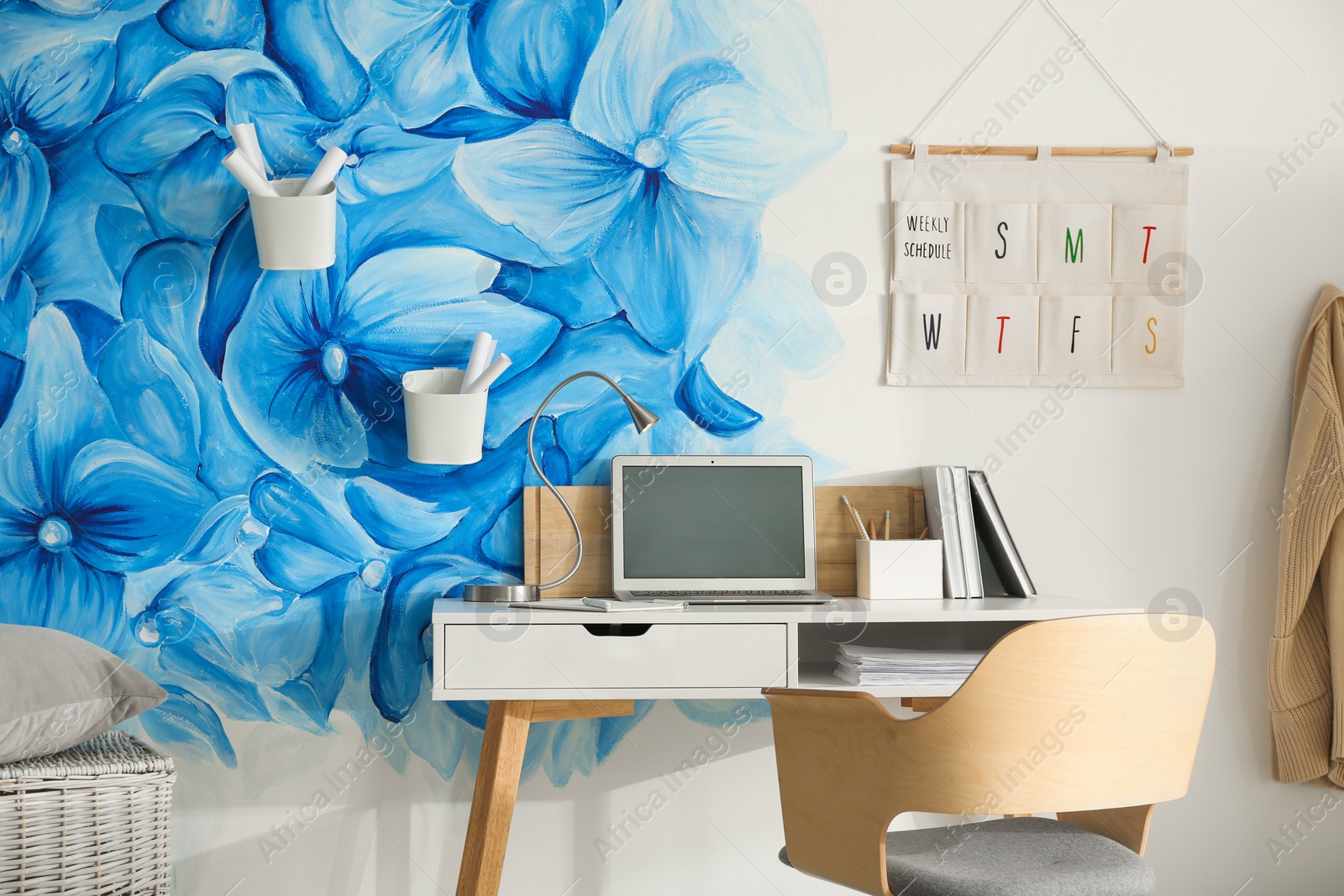 Photo of Stylish workplace with blue flowers painted on wall. Floral pattern in living room interior