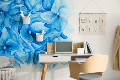 Photo of Stylish workplace with blue flowers painted on wall. Floral pattern in living room interior