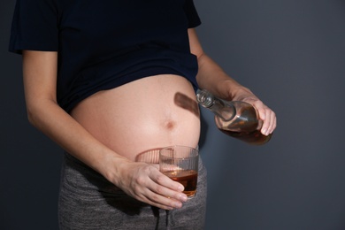 Photo of Pregnant woman pouring whiskey into glass on dark background. Alcohol addiction