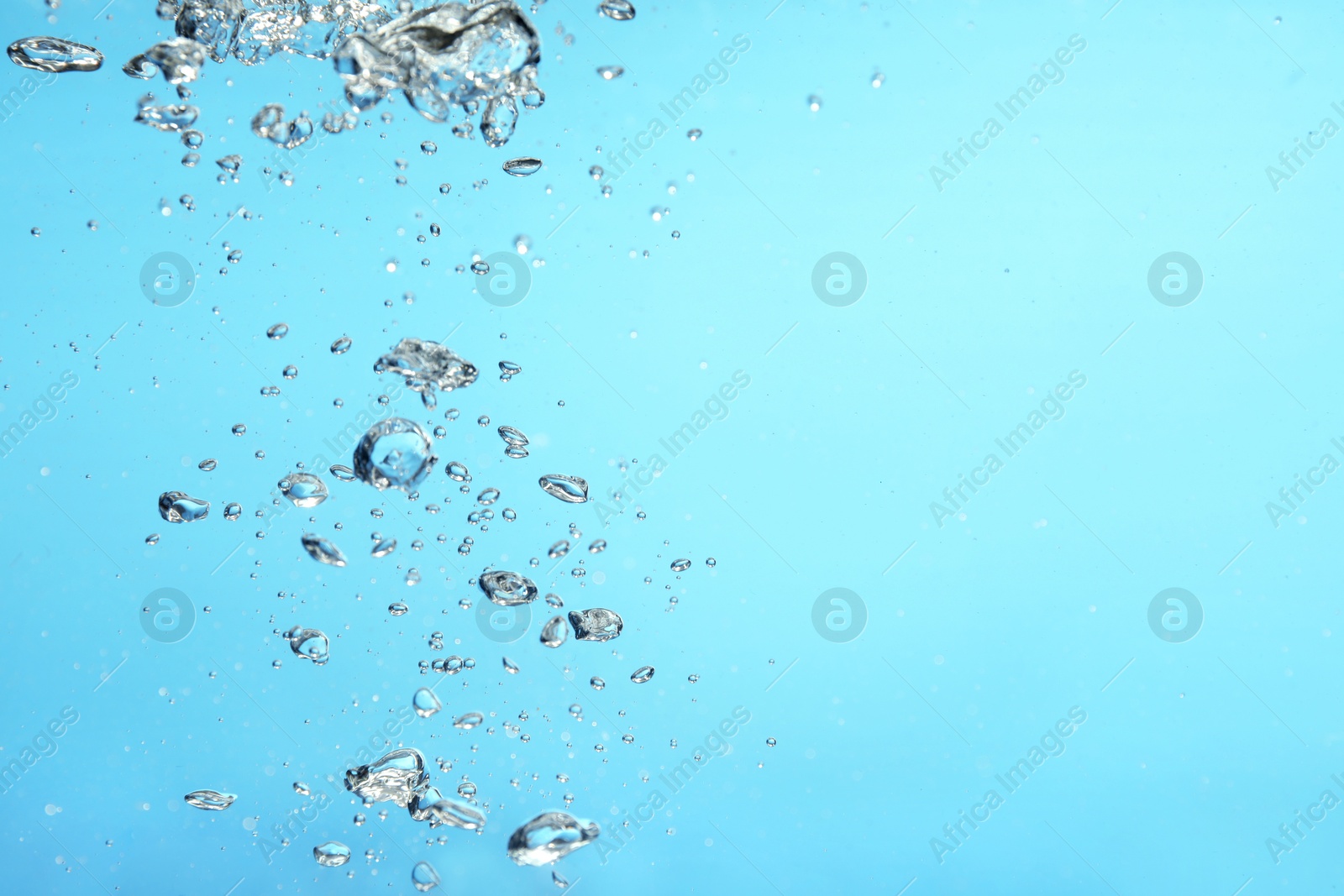 Photo of Air bubbles in water on light blue background. Space for text