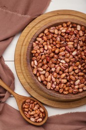 Photo of Bowl and spoon with dry kidney beans on white table, flat lay