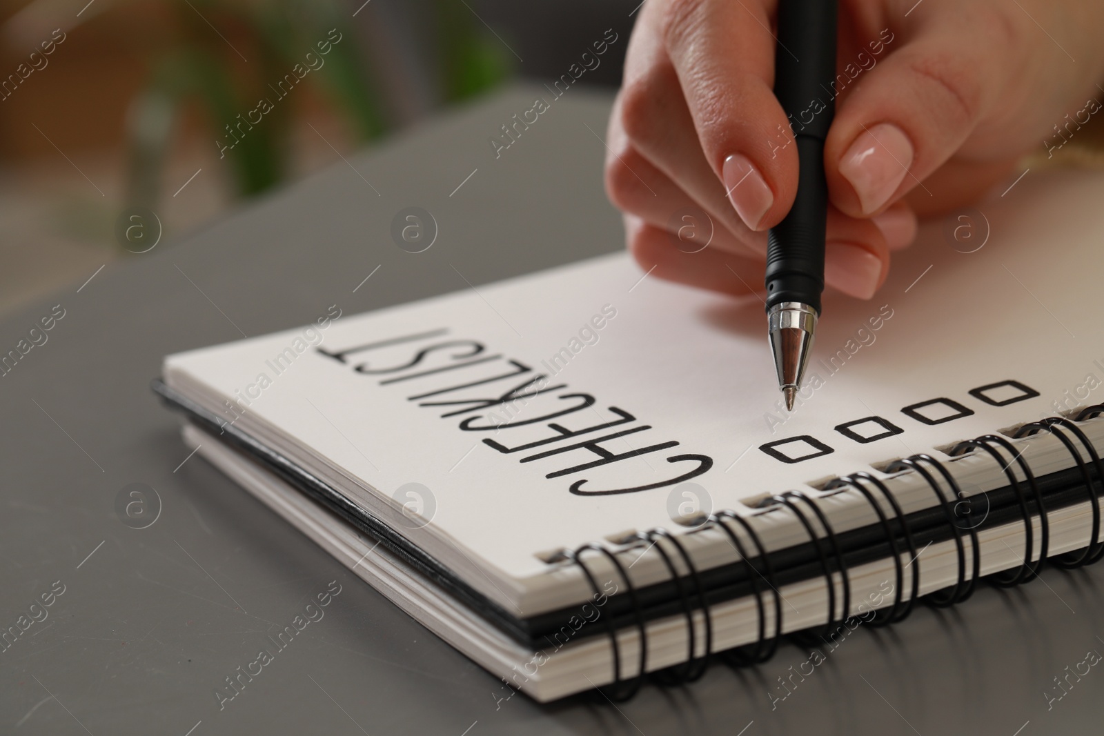 Photo of Woman filling Checklist with pen at grey table, closeup