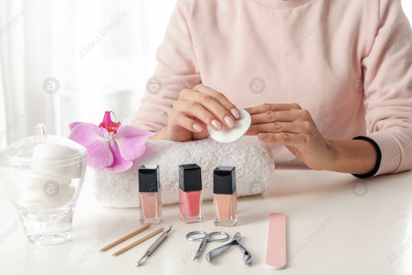 Photo of Woman removing polish from nails with cotton pad at table, closeup