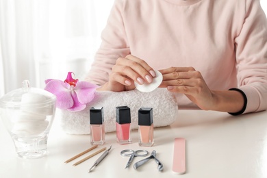 Photo of Woman removing polish from nails with cotton pad at table, closeup