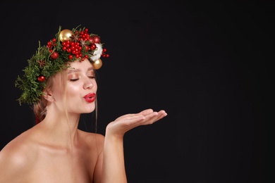 Photo of Beautiful young woman wearing Christmas wreath on black background. Space for text