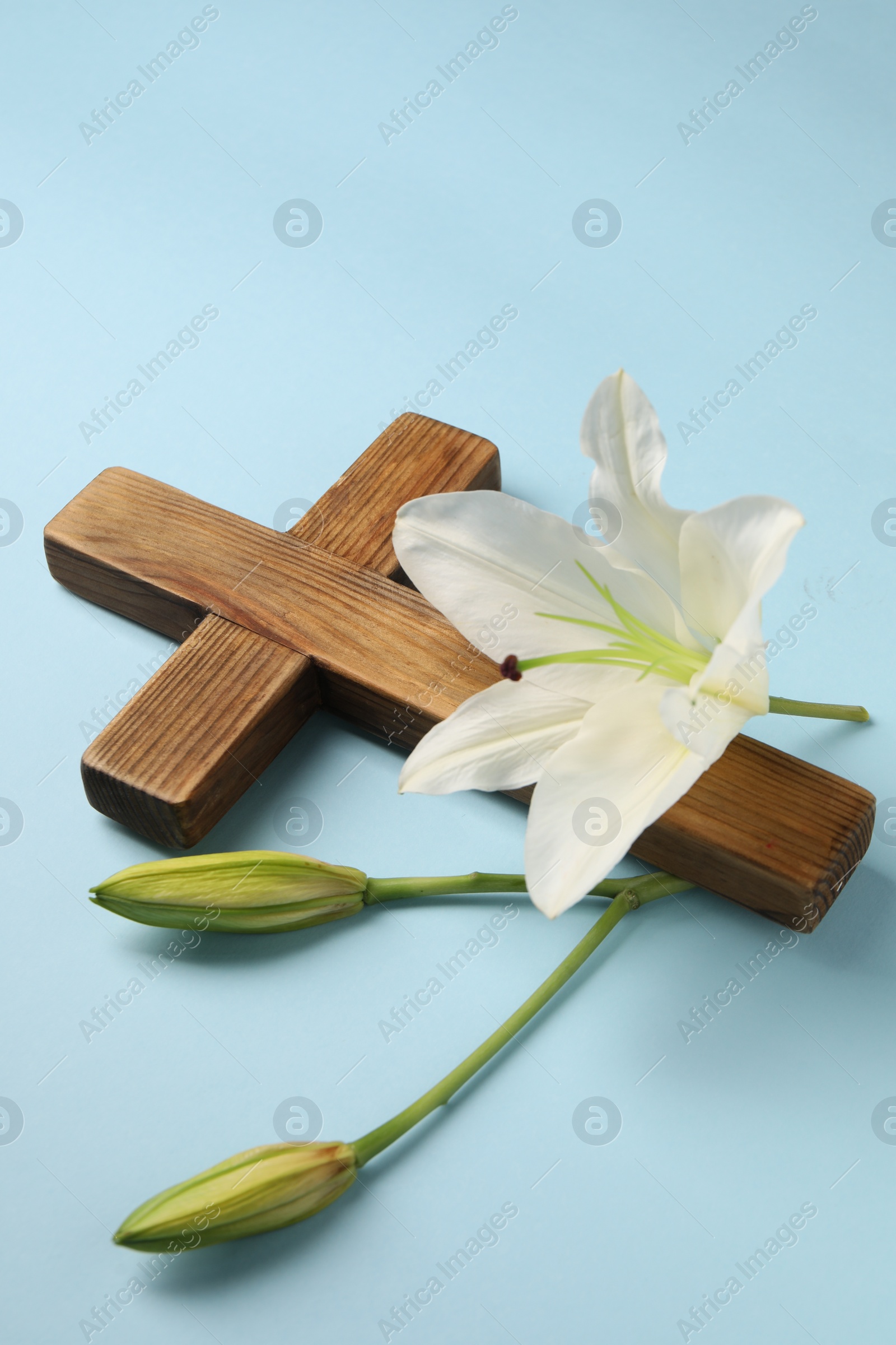 Photo of Wooden cross and lily flowers on light blue background. Easter attributes