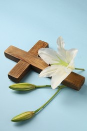 Wooden cross and lily flowers on light blue background. Easter attributes