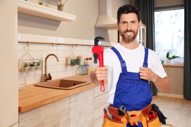 Plumber with pipe wrench and tool belt in kitchen, space for text