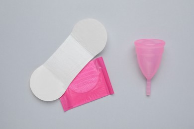 Photo of Menstrual cup and disposable pantyliners on grey background, flat lay