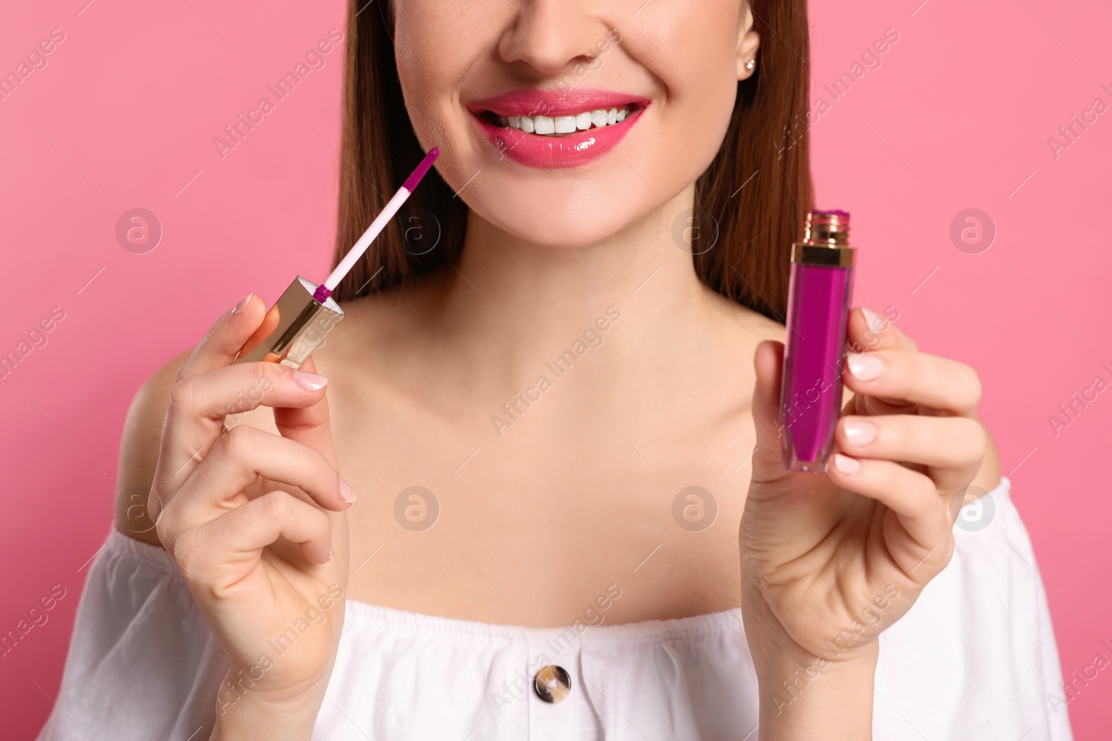 Photo of Beauty blogger applying lipgloss on pink background, closeup