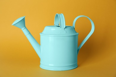 Turquoise metal watering can on yellow background