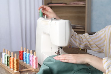 Photo of Seamstress working with sewing machine at wooden table indoors, closeup