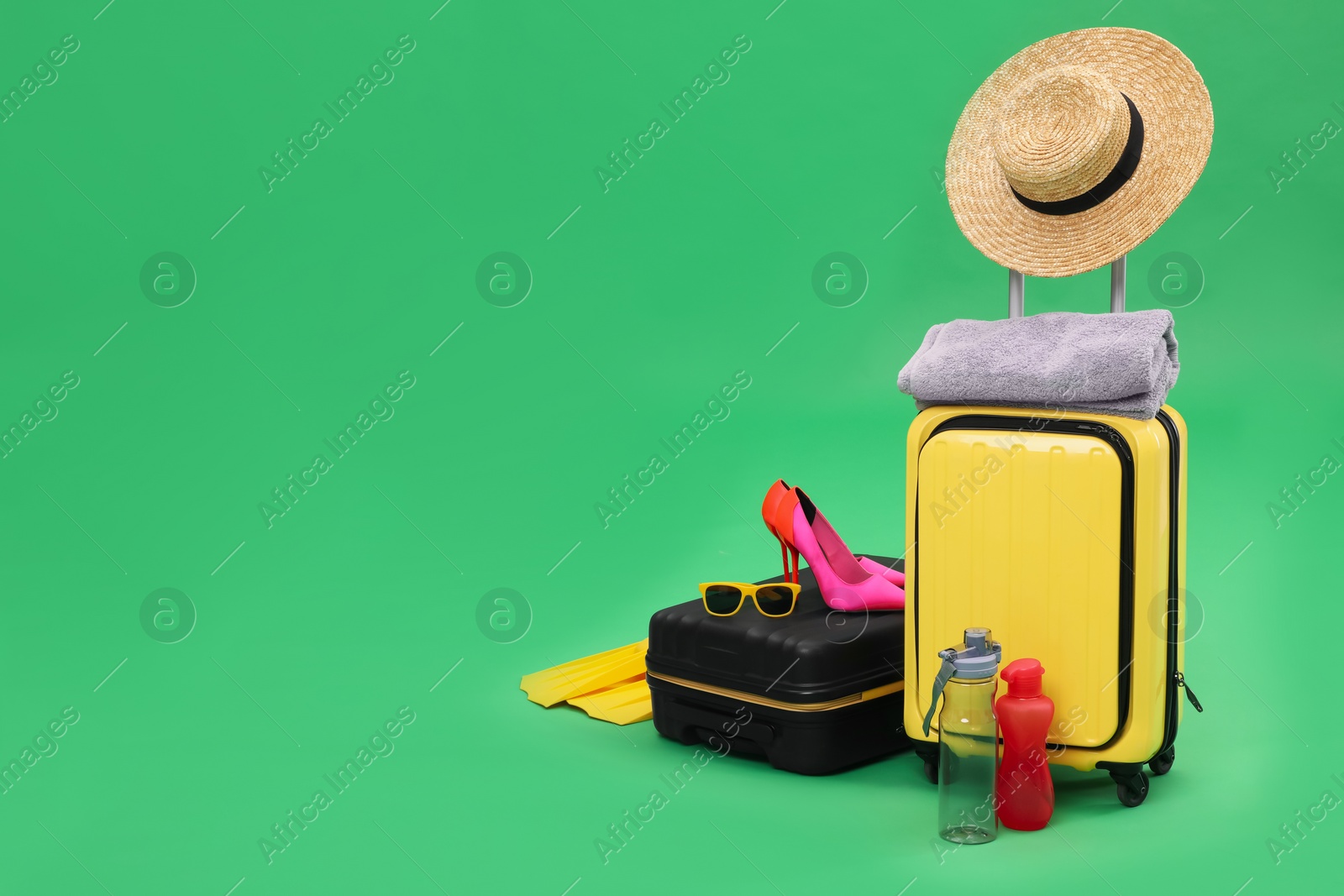 Photo of Suitcases, bottles and beach accessories on green background, space for text. Summer vacation